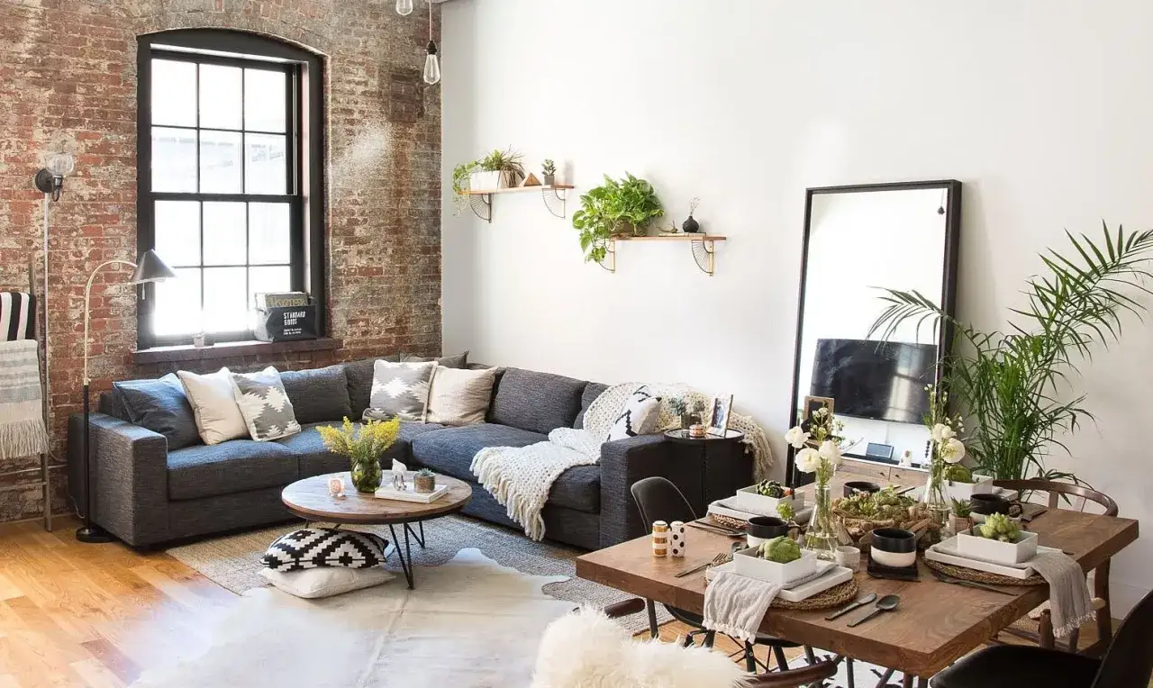 Acogedor salón con sofá gris, mesa de centro de madera y comedor. Interiores de casas sencillas con ladrillo visto y plantas.