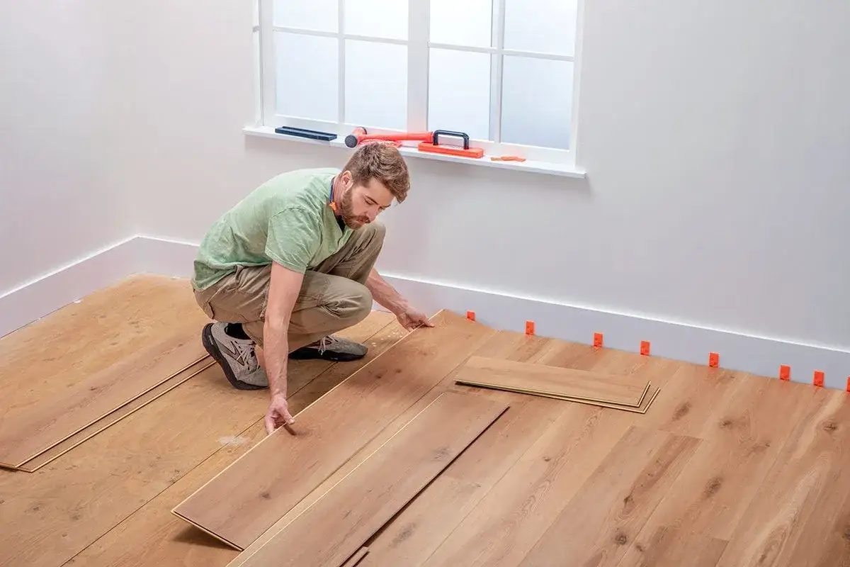 Hombre instalando tablas de madera para poner suelo vin&iacute;lico. Se ven cu&ntilde;as naranjas en el rodapi&eacute;.