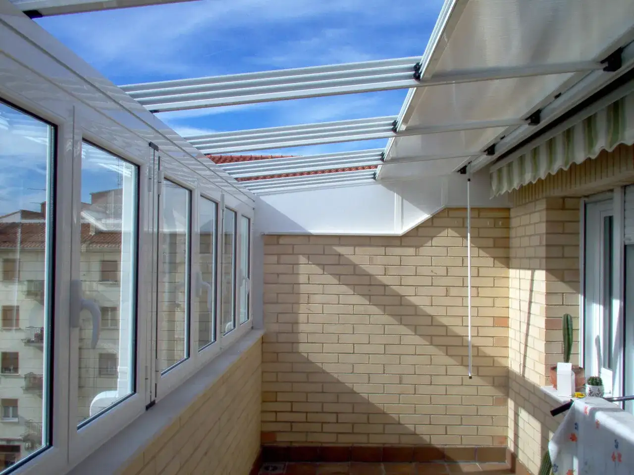 Techo corredizo panel s&aacute;ndwich sobre una terraza acristalada, con vistas a edificios y cielo azul.
