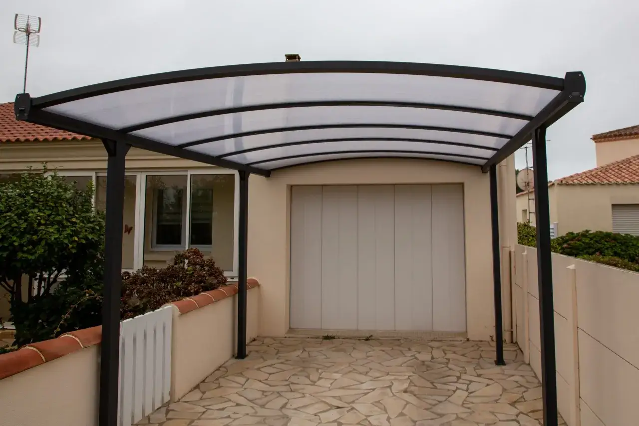 Monteras para patios modernas, con techo curvo de policarbonato y estructura met&aacute;lica negra, protegiendo una entrada de garaje.