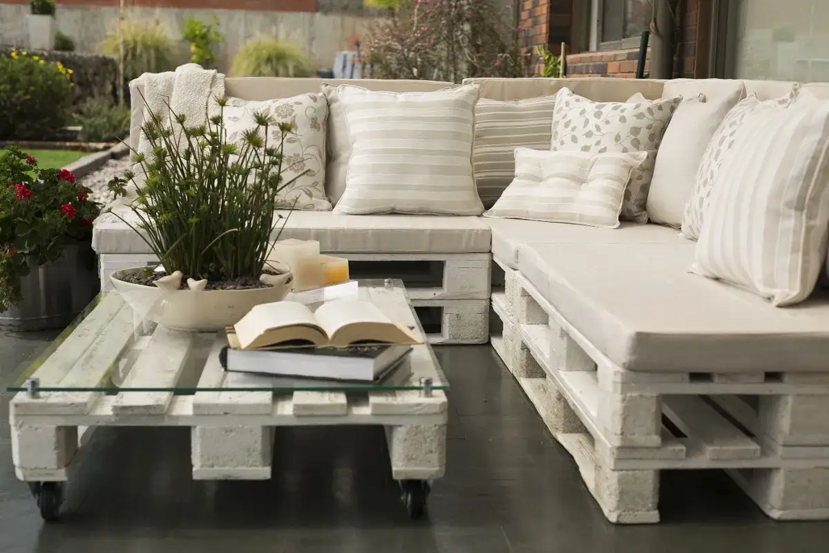 Sof&aacute; y mesa de centro hechos con palets, con cojines claros y plantas. &iexcl;Ideas con palets para un espacio exterior acogedor!