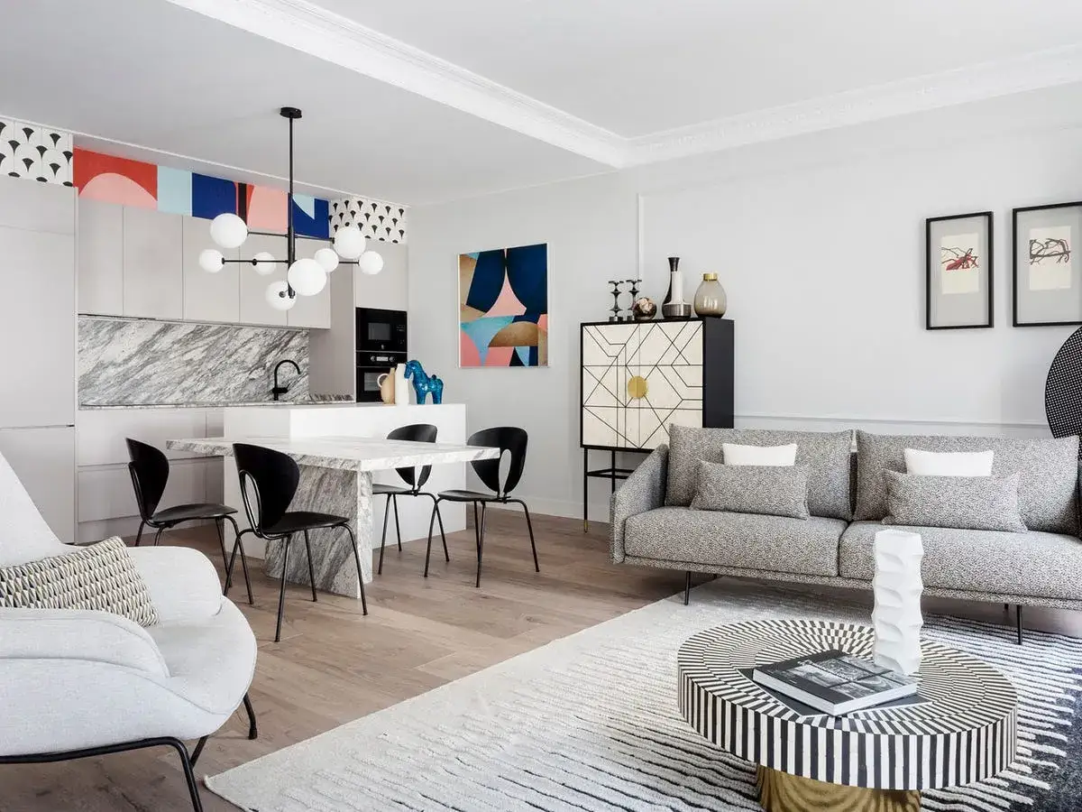 Un sal&oacute;n-comedor moderno y luminoso, ideal para mini pisos. Destaca una isla de cocina con encimera de m&aacute;rmol, un sof&aacute; gris y una mesa de centro geom&eacute;trica.