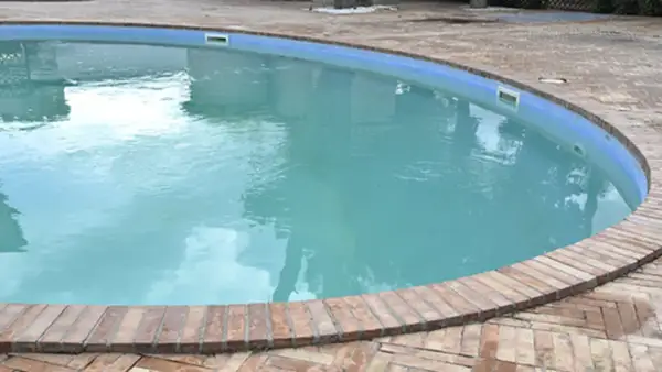 Agua de piscina blanquecina, con reflejos del cielo y rodeada por un borde de ladrillos.