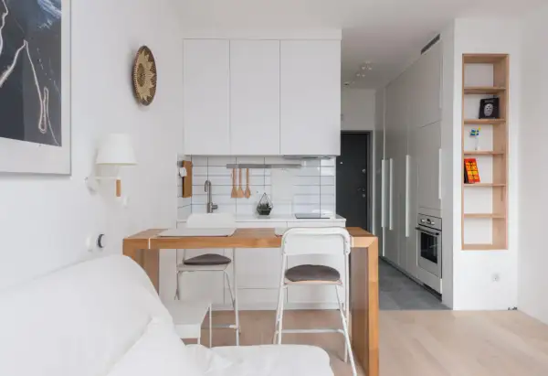 Interiores de casas sencillas con cocina blanca, barra de madera y sofá blanco. Estilo minimalista y funcional.