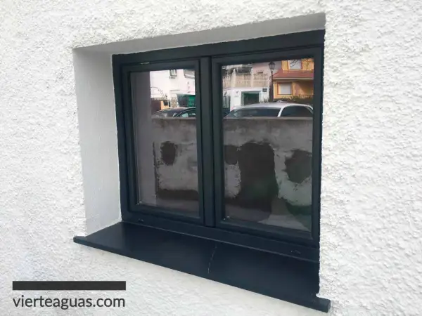 Ventana con marco oscuro y un alféizar negro que funciona como vierteaguas, protegiendo la pared de la lluvia.