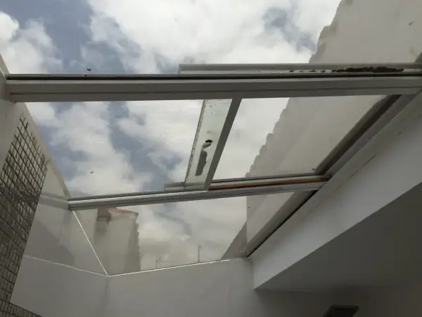 Techos de cristal inconvenientes: suciedad y óxido en los marcos, reflejando un cielo nublado y edificios.