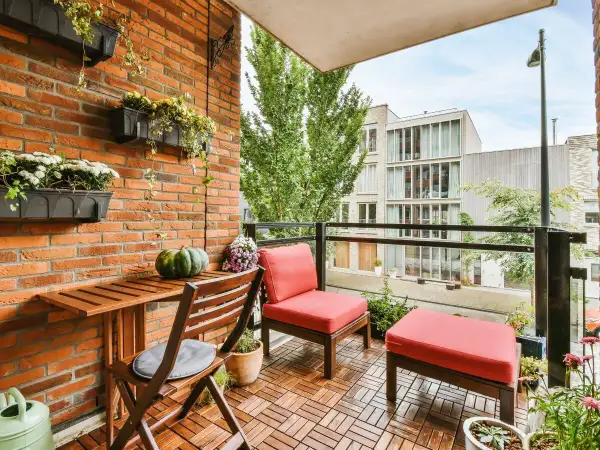 Un balcón alargado decorado con muebles de madera, cojines rojos y plantas colgantes. Un espacio acogedor para disfrutar del exterior.