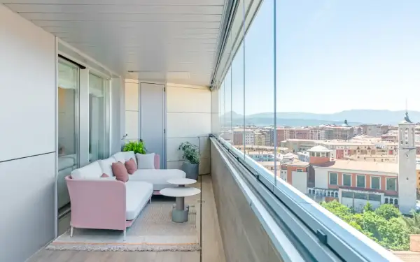 Sofá rosa y blanco en terrazas acristaladas con decoración moderna. Disfruta de la vista urbana desde este espacio acogedor.