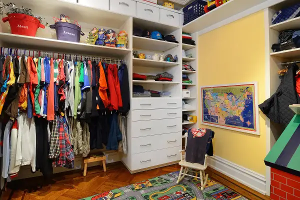 Armario infantil con ropa colgada en la barra, estantes con juguetes y cajones. La altura de la barra del armario es perfecta para los niños.