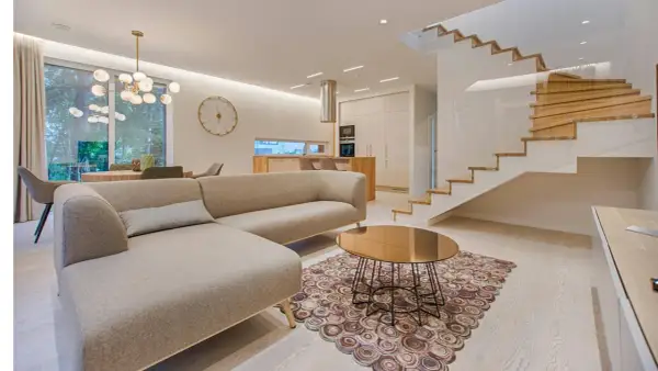 Elegantes ideas de interiores de casas: sofá moderno, mesa de centro dorada, alfombra circular y escaleras de madera flotantes.