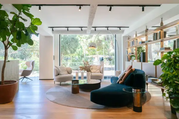 Amplio salón con sofás curvos, sillones, mesas de centro y estanterías, todo bañado por luz natural a través de grandes ventanas modernas.