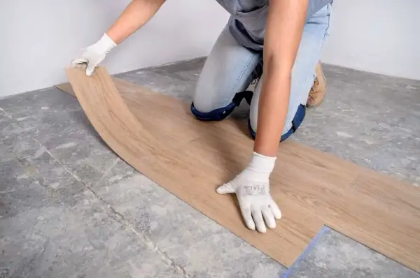 Manos enguantadas colocando una tabla de suelo vinílico sobre un suelo de hormigón.