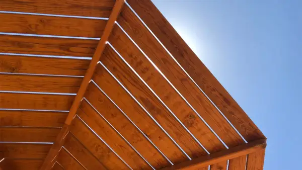 Vistas desde abajo de una estructura de madera con tratamiento para exterior, con el cielo azul brillante entre las lamas.