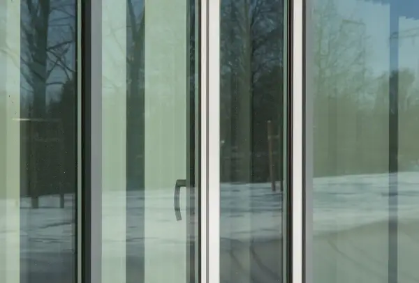 Ventana con cristal planitherm, reflejando árboles y nieve. Un tirador plateado se ve en el panel central.