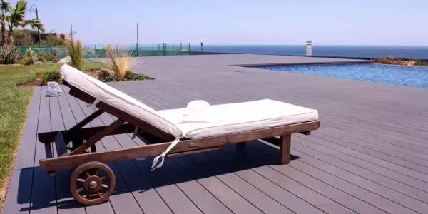 Tumbona lista para el sol sobre una terraza de madera composite, con piscina y mar al fondo.