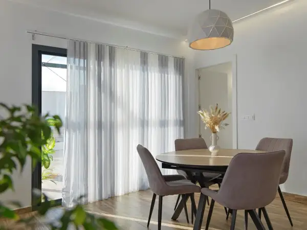 Comedor moderno con mesa y sillas, y diferentes tipos de cortinas que filtran la luz.