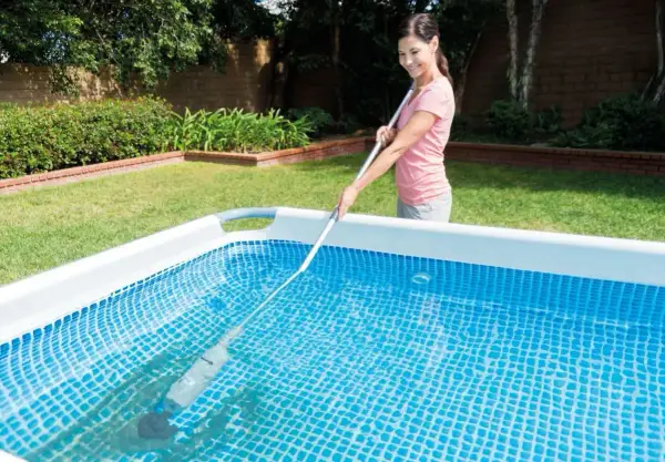 Mujer sonriente realizando el mantenimiento de piscinas con un limpiafondos.